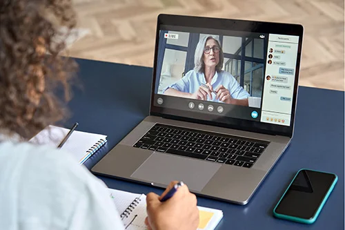 eine Frau sitzt an einem Tisch mit einem Laptop vor orangenem Hintergrund