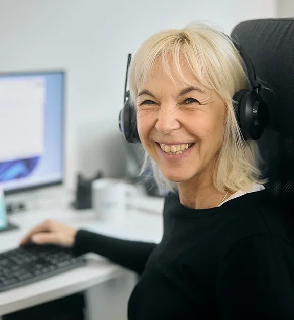 Frau mit Headset sitzt am PC und lächelt