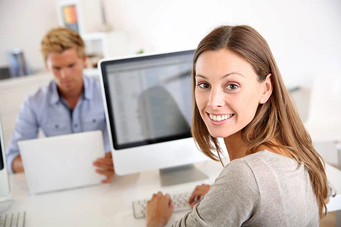 eine Frau, die an einem Schreibtisch mit einem Computer sitzt. Ihr gegenüber ein Mann mit einem Tablet