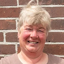 Die stolze Weiterbildungsteilnehmerin Astrid Estel steht, die Hände auf die Hüften gestützt, vor einer geziegelten Hauswand.