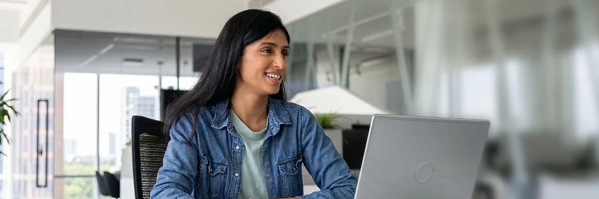 Junge Frau mit braunen langen Haaren sitzt lächelnd vor einem Laptop