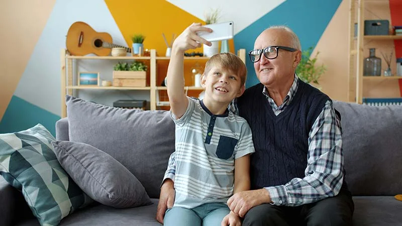 Junge macht ein Selfie von sich und seinem Opa auf dem Sofa.